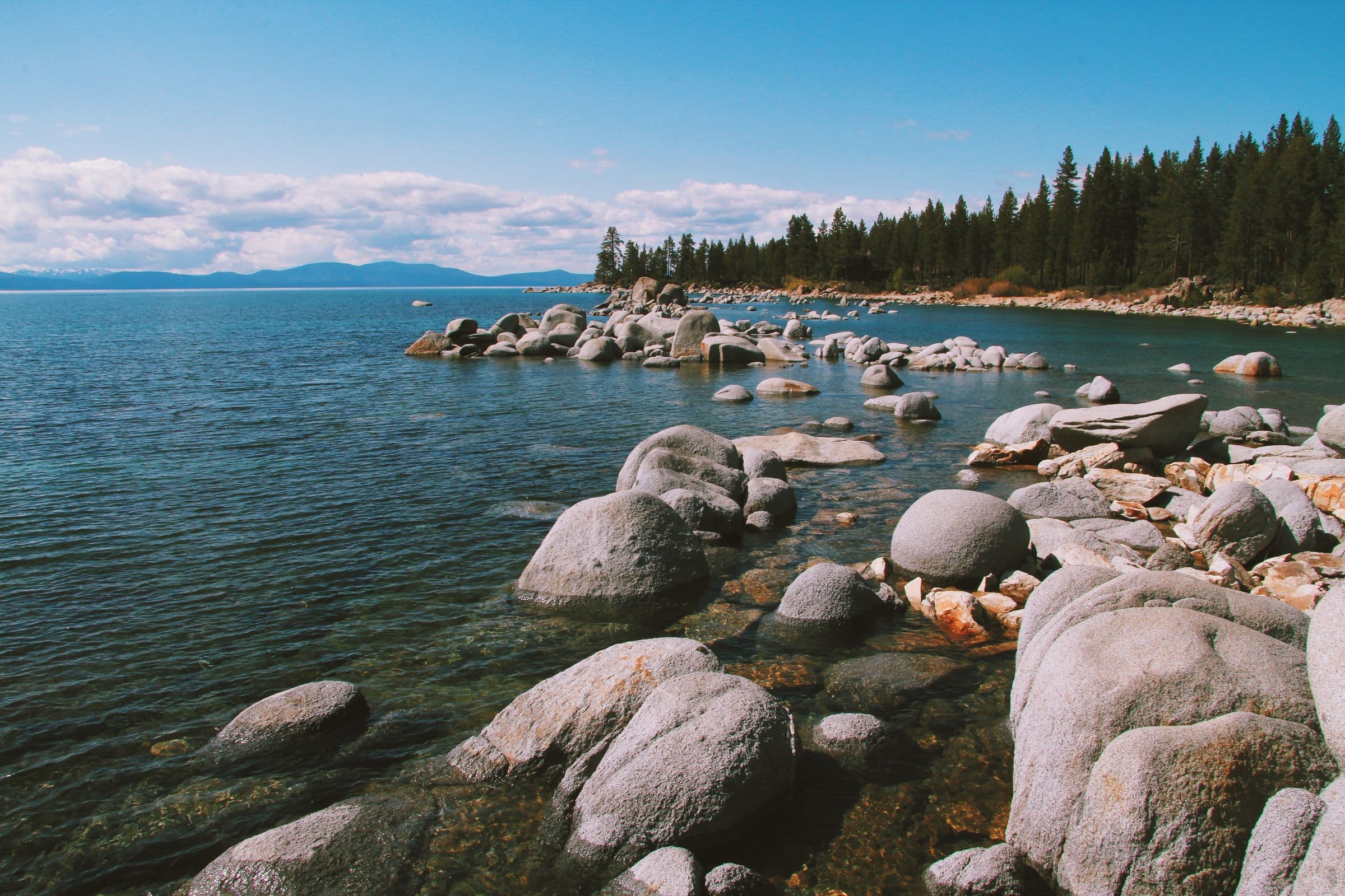 Granite boulders along the clear blue shoreline of Lake Tahoe under a bright sky